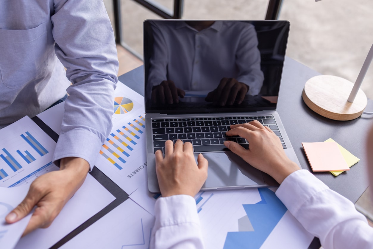 Team businesspeople or an accountant team are analyzing data charts, graphs, and a dashboard on a laptop screen in order to prepare a statistical report and discuss financial data in an office. Team of financial planners working together at a desk on investment management with a portfolio and computer in front of them